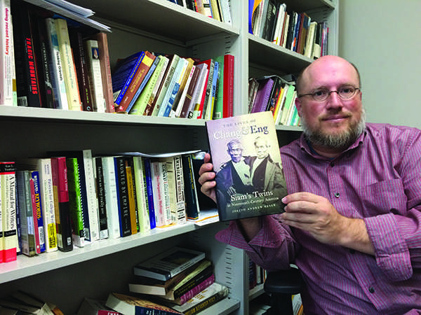 UW-Eau Claire professor of English and history Joe Orser poses with his recently published book, The Lives of Chang and Eng: Siams Twins in Nineteenth Century America. The text, published by the University of North Carolina Press, will be celebrated by the university community at a book signing event at 6 p.m. Monday in the Menominee Room of Davies Center. - Photo by Courtney Kueppers