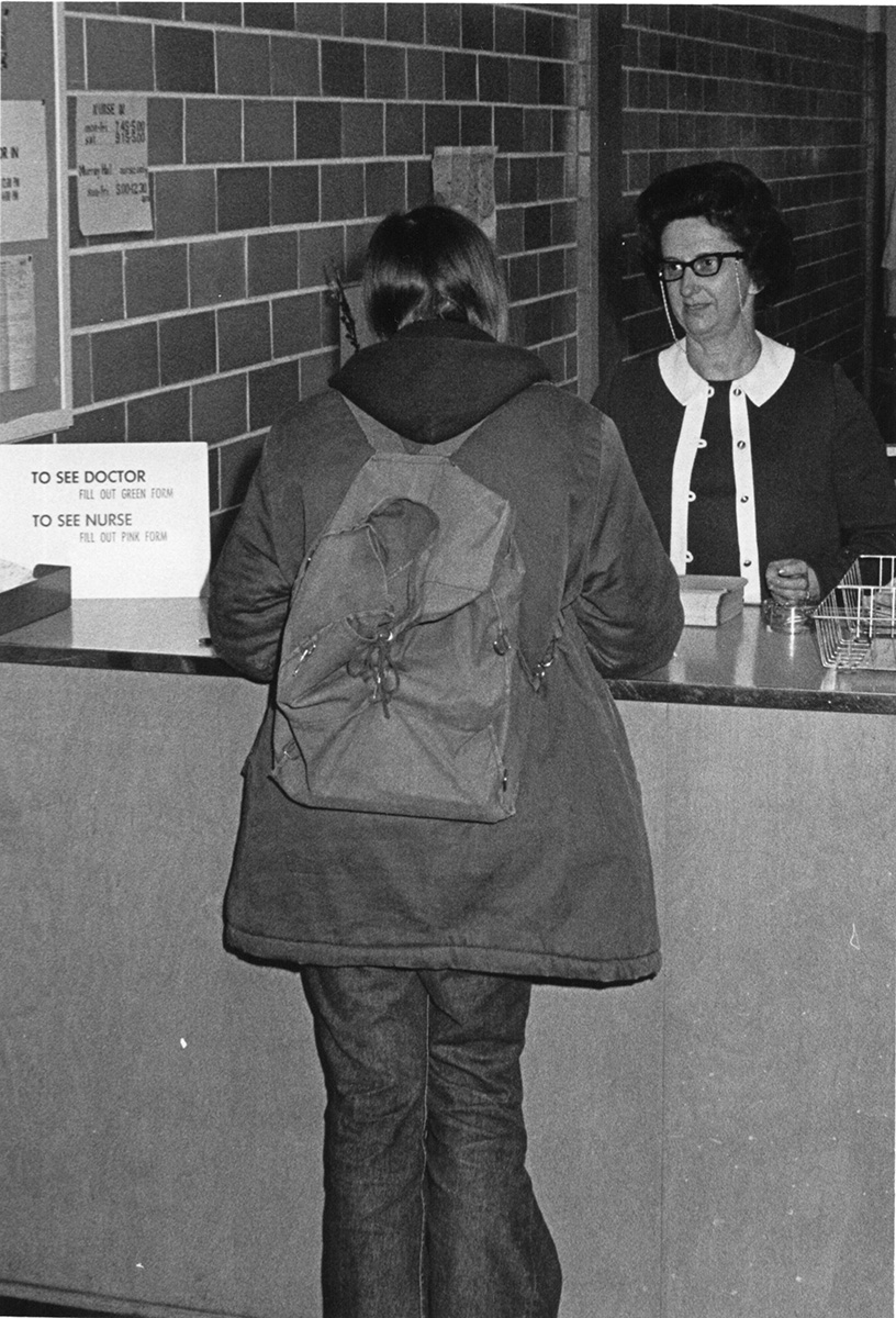 A student stands at the reception desk of the campus health center, circa 1960s.