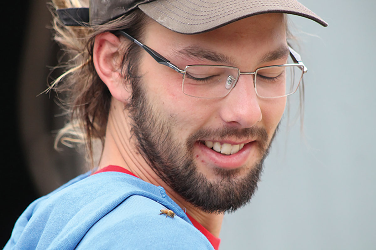 Kristof White smiles down on one of the thousands of bees he cares for on his bee farm in Augusta, Wisconsin.