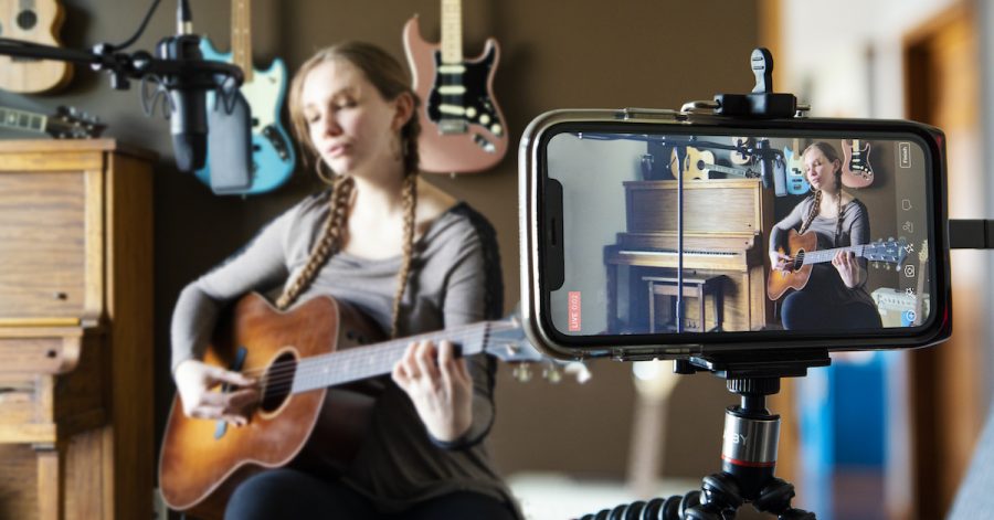 A smartphone recording a woman playing guitar.