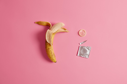 Condom tested on banana. Effective preventing pregnancy product for your safety. Unplanned parenthood. Standard size. Pink background. Contraceptive with banana flavor. Birth control, contraception